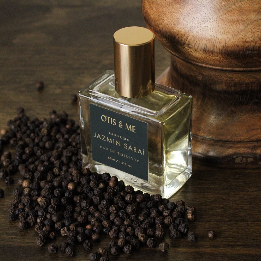 Bottle of perfume with black peppercorns around it.