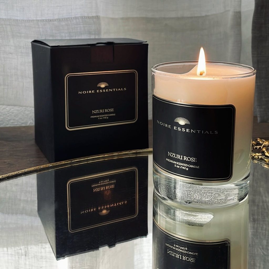 lit candle in a glass votive sitting on a mirrored tray with the candle box beside it. The label says Noire Essentials, Nzuri Rose